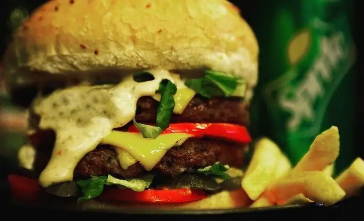 تصویری نزدیک از همبرگر دوبل ویژه فست فود وسپا برگر با پنیر، کاهو و سس، کنار سیب زمینی و نوشابه Sprite.