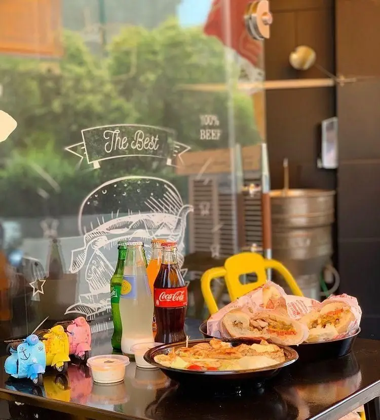 نمایی از میز فست فود وسپا برگر با ساندویچ‌های لذیذ، غذای گرم، نوشیدنی و ماکت‌های وسپا، فضایی دلنشین و خوشمزه.