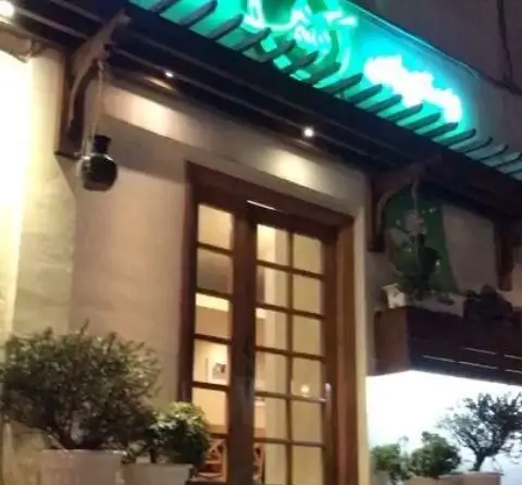 نمای بیرونی شبانه رستوران شمالی گیله گل با درب چوبی شیک، تابلوی نئون سبز و گلدان‌های تزئینی. محیط دنج و سنتی.