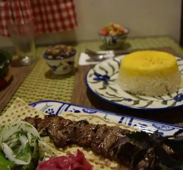تصویری از میز غذا در رستوران شمالی گیله گل شامل کباب لذیذ با برنج زعفرانی و مخلفات اصیل، انتخابی عالی برای غذای گیلانی