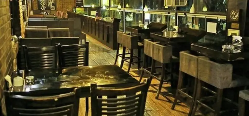 فضای داخلی کافه خانه هنرمندان با دکوراسیون گرم و صمیمی، شامل میز و صندلی‌های ناهارخوری و کانترهای بلند. محیطی دنج و ایده‌آل برای دورهمی‌ها.