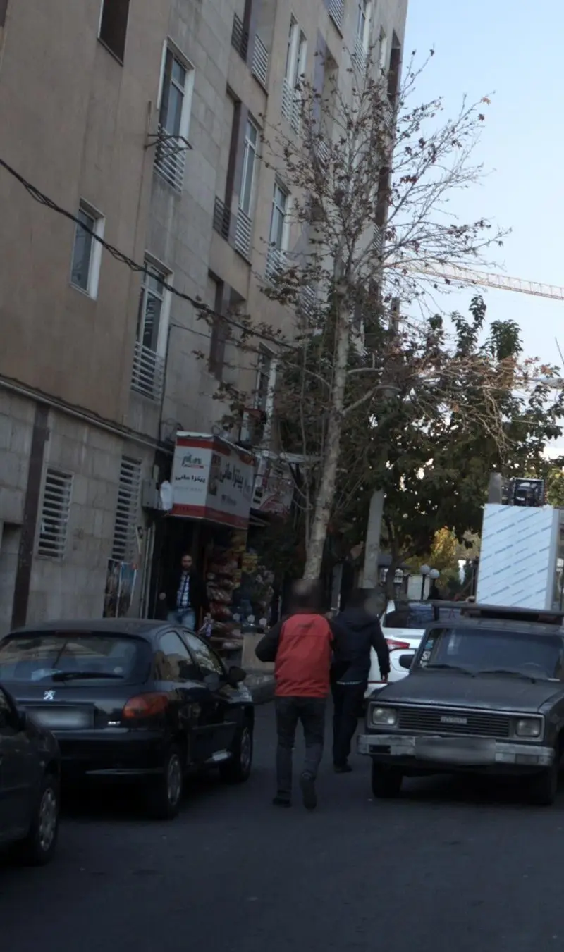 نمای بیرونی پیتزا مانی در محیطی شهری با ساختمان‌های بلند، خودروهای پارک شده و عابران پیاده در خیابان.