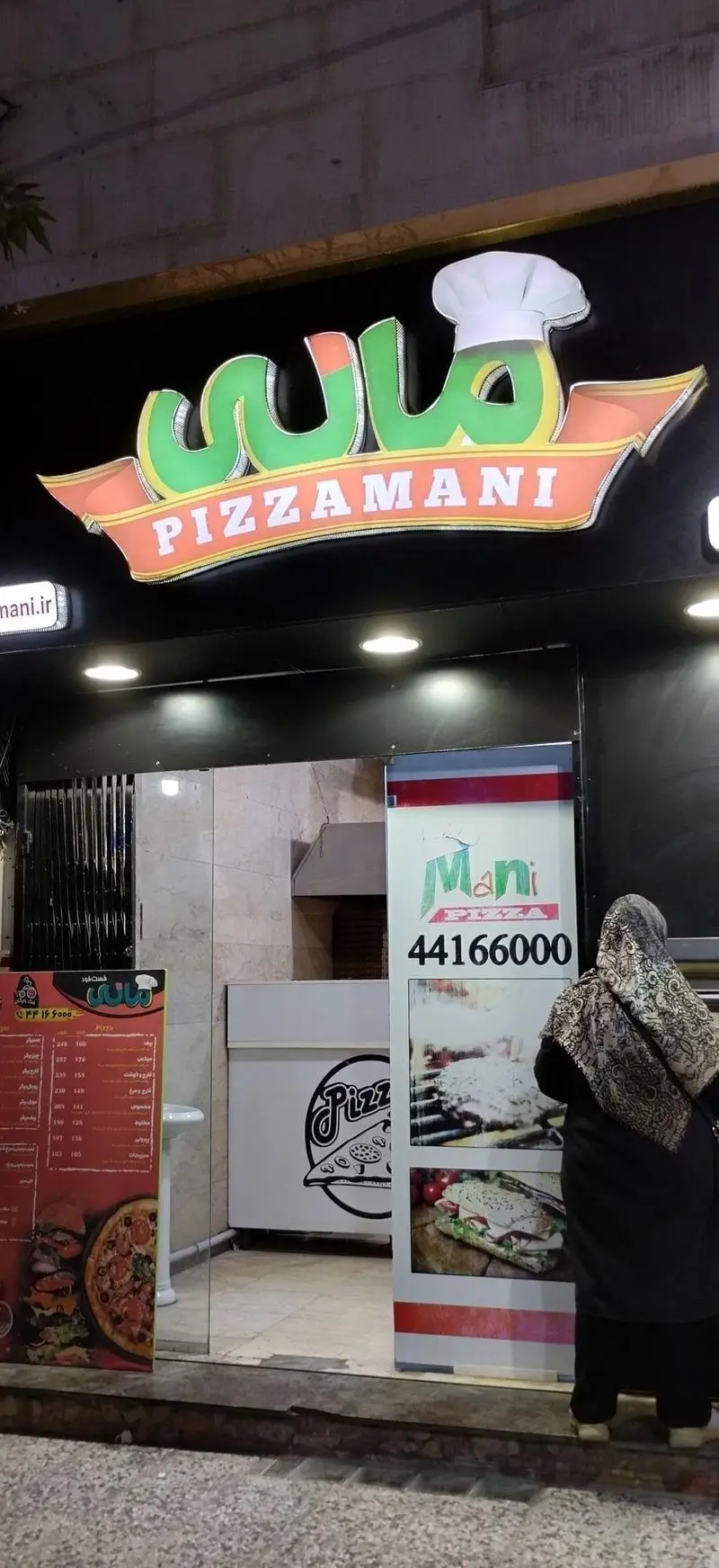نمای بیرونی شبانه فست فود پیتزا مانی با تابلوی جذاب و لوگوی سرآشپز، منوی کامل غذاها و اطلاعات تماس از جمله وبسایت pizzamani.ir