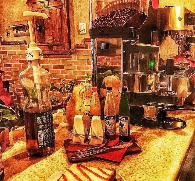 تصویری از پیشخوان کافه پندار: دستگاه اسپرسو، دانه‌های قهوه، سیروپ، دکور پاییزی کدو و دسری لذیذ برای تجربه ای دلنشین در کافه.