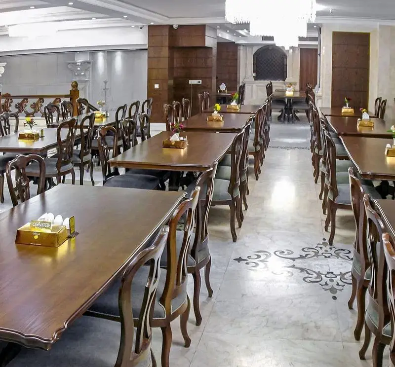 نمایی از فضای داخلی رستوران اقدسیه، شامل ردیف های منظم میز و صندلی های چوبی شیک، با دکوراسیون مجلل و نورپردازی زیبا.