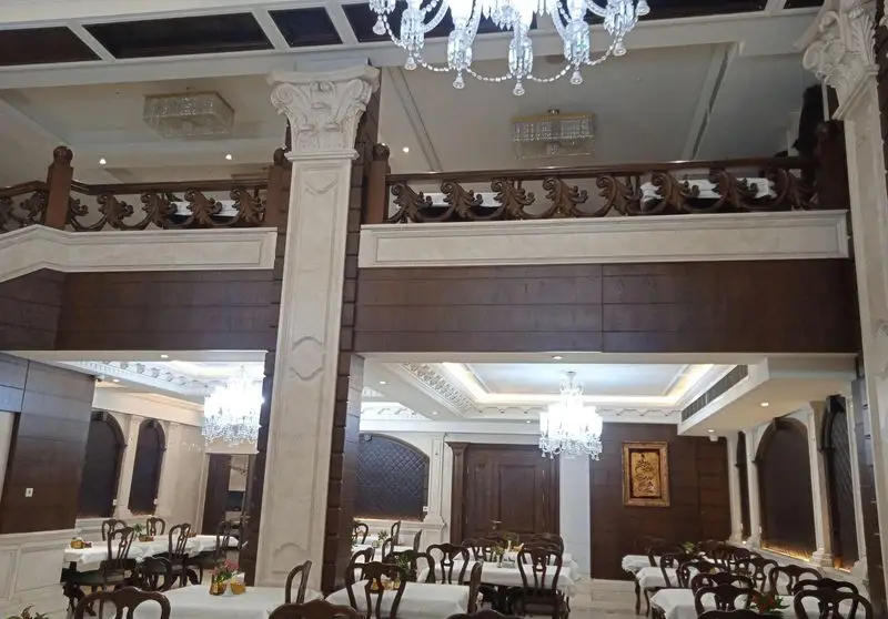 فضای داخلی شیک و لوکس رستوران اقدسیه با میزهای چیدمان شده، صندلی‌های چوبی و لوسترهای کریستالی در سالن غذاخوری دوطبقه.