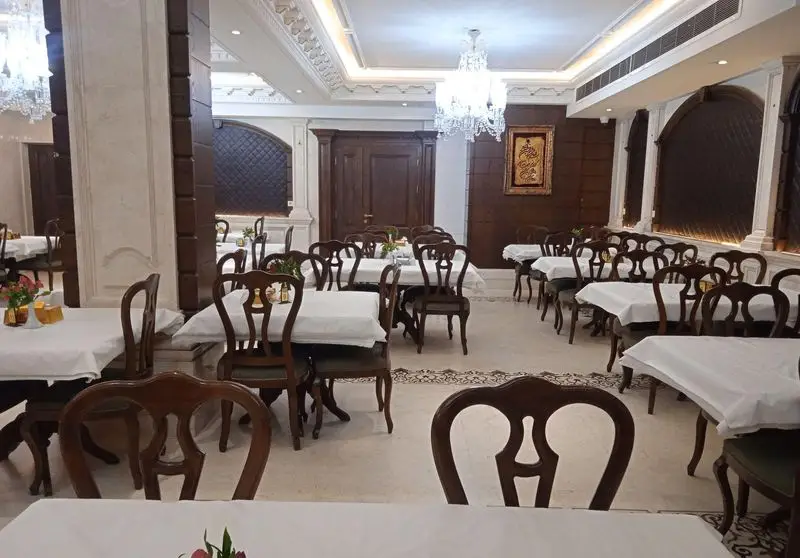 فضای داخلی دلباز و چیدمان لوکس رستوران اقدسیه با میز و صندلی‌های چوبی کلاسیک، رومیزی‌های سفید و نورپردازی شیک.