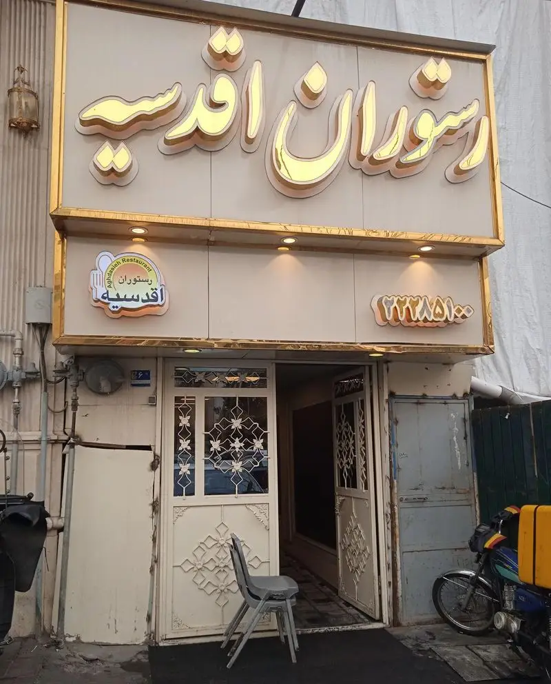 نمای جلویی رستوران اقدسیه در تهران، با تابلوی شیک طلایی و ورودی باز. آماده ارائه لذیذترین غذای ایرانی برای مهمانان و تحویل.