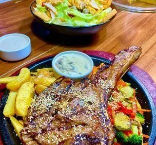 استیک تاماهاک آبدار با سس مخصوص، سیب زمینی سرخ کرده و سبزیجات تازه در کافه رستوران ایتالیایی مدس، همراه با سالاد.