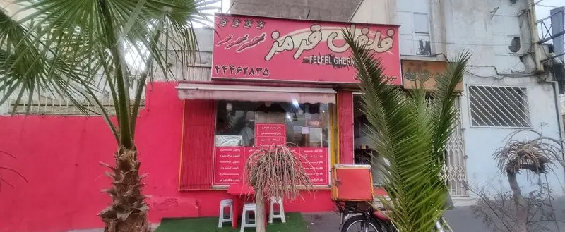 نمای بیرونی فست فود فلفل قرمز (Feleel Gherm) با رنگ قرمز جذاب، تابلوی روشن، درختان نخل و دوچرخه دلیوری، تلفن ۴۴۴۶۲۸۳۵.