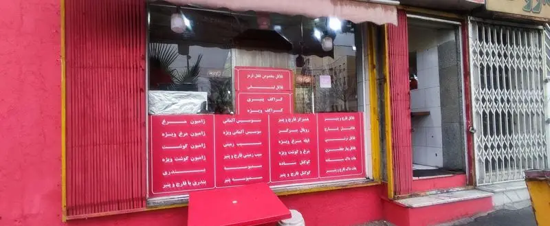 نمای بیرونی روشن فست فود فلفل قرمز، با ویترین حاوی منوی کامل اغذیه شامل فلافل، ساندویچ و هات داگ.