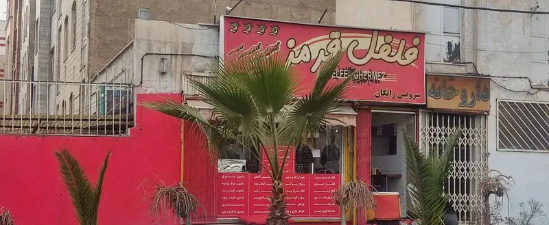 نمای بیرونی فست فود فلفل قرمز با تابلوی قرمز رنگ، همراه با سرویس رایگان و درخت نخل در جلوی مغازه، در یک روز ابری.