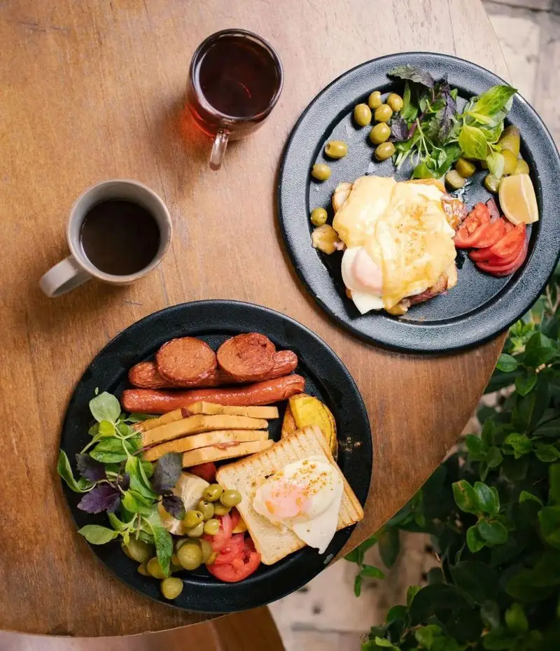 صبحانه کامل و لذیذ در کافه رستوران دایموند شامل املت بندیکت، سوسیس، تخم مرغ، زیتون، نان تست، قهوه و چای روی میز چوبی.