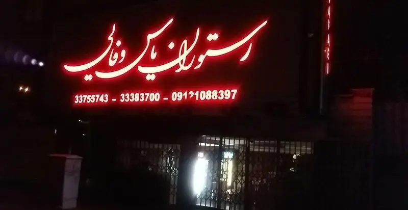 تابلوی نئون قرمز رستوران یاس وفایی در شب، به همراه شماره تلفن‌های 33755743، 33383700 و 09121088397.
