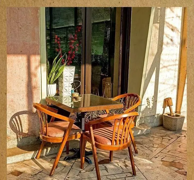 فضای دنج و هنری کافه خانه فرهنگ و هنر سرهنگ با میز و صندلی چوبی و نور آفتاب، مکانی عالی برای استراحت و گفتگو.