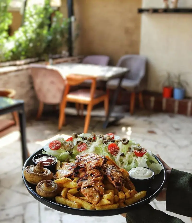 غذای خوشمزه و سالم در خانه فرهنگ و هنر سرهنگ: بشقاب مرغ گریل، سیب زمینی، قارچ و سالاد تازه در فضای دلنشین کافه.