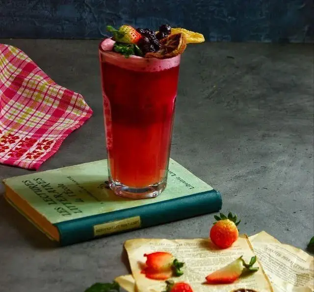 یک نوشیدنی میوه‌ای خاص و تازه با تزئین توت‌فرنگی و بلوبری، روی کتابی قدیمی در کافه هنری خانه فرهنگ و هنر سرهنگ.