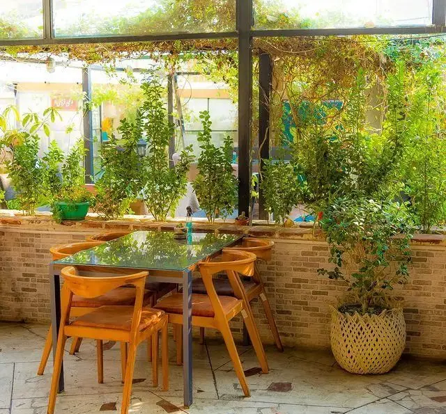 فضای سرسبز و دلنشین کافه خانه فرهنگ و هنر سرهنگ با میز و صندلی‌های چوبی، ایده‌آل برای آرامش و دورهمی‌های فرهنگی هنری.