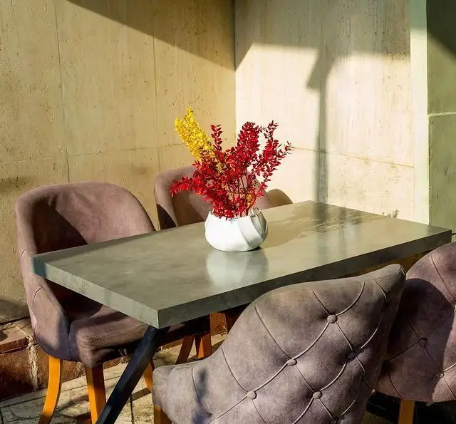 فضای داخلی خانه فرهنگ و هنر سرهنگ با میز بتنی، صندلی‌های شیک و گلدان زیبا با شاخه‌های قرمز و زرد، مناسب پاتوق‌های فرهنگی.