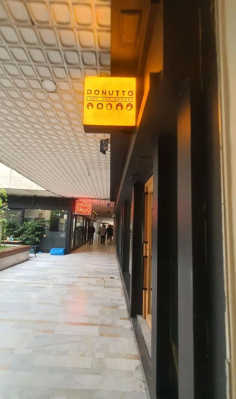نمای بیرونی کافه و نانوایی دوناتو با تابلوی درخشان و لوگوی دونات. این کافه با فضای مدرن در یک گذرگاه پیاده‌رو شلوغ قرار دارد.