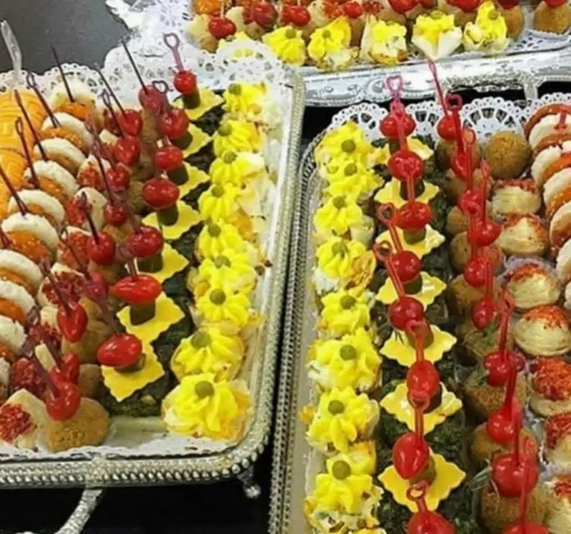 سینی‌های مجلل فینگر فود و مزه‌های متنوع از هنرکده کارامل، شامل کاناپه‌های رنگی، دسرهای کوچک و شیرینی‌های شیک برای پذیرایی.