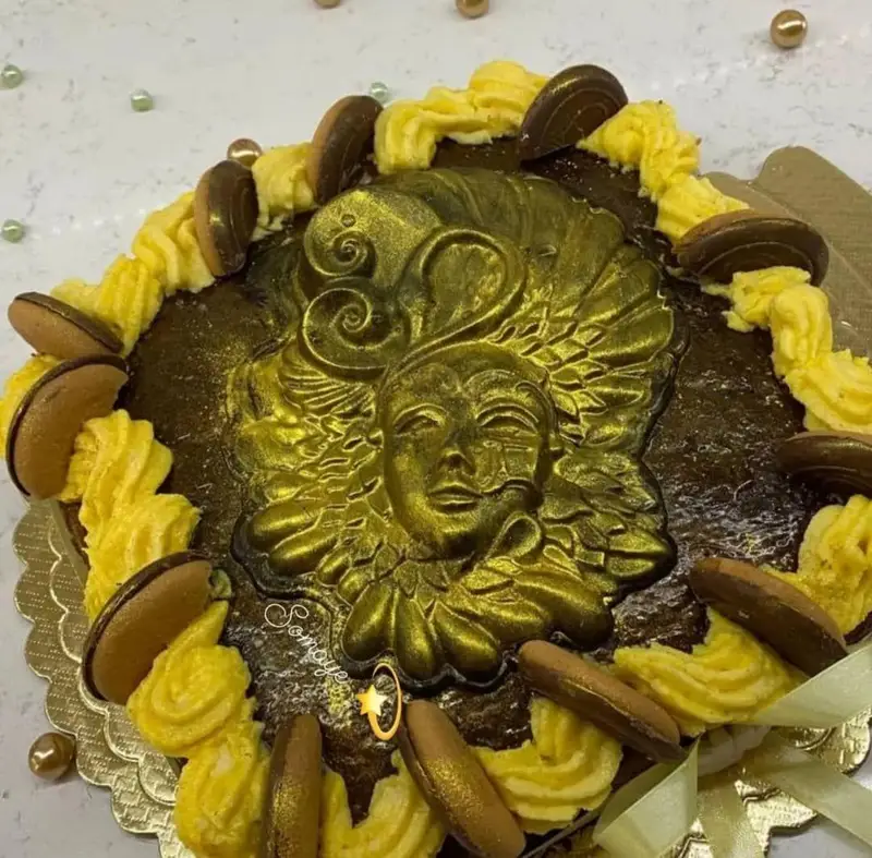 کیک جشن خاص شکلاتی هنرکده کارامل با تزئین ماسک برجسته طلایی، خامه زرد و بیسکوییت بیضی شکل. عالی برای رویدادها.