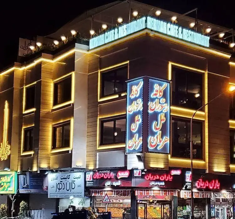 نمای بیرونی کافه رستوران هرمان در شب با نورپردازی طلایی و مدرن. ساختمانی چند طبقه و جذاب در دل شهر.