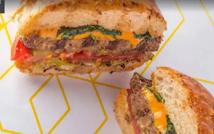 ساندویچ بزرگ و لذیذ فریکادل نصف شده با نان تست شده، نمایش دهنده لایه های گوشت، پنیر طلایی، کاهو، گوجه و خیارشور، فست فود فریکادل.