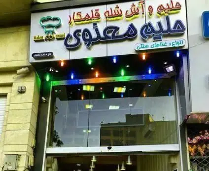 نمای بیرونی آش و حلیم پزی حاج علی معنوی و پسران با تابلوی روشن؛ عرضه انواع حلیم، آش شله قلمکار و غذاهای سنتی.