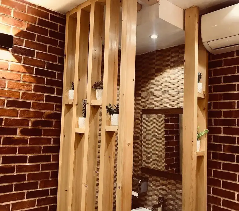 طراحی داخلی خاص پیتزا تنوری پاروت: دیوارهای آجری، پارتیشن چوبی با گلدان‌های زینتی و آینه، ایجاد فضایی دلنشین و مدرن.