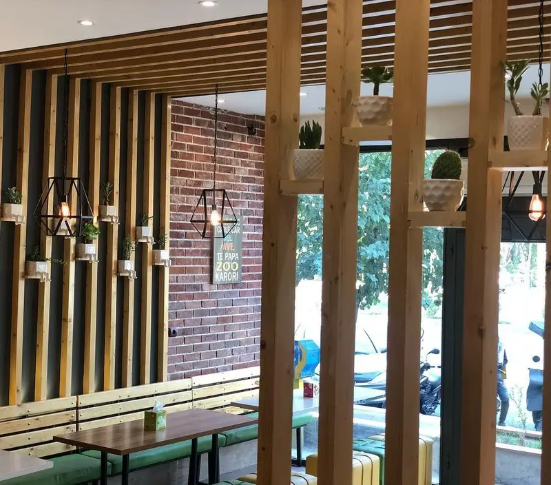 تصویر دکوراسیون داخلی رستوران پیتزا تنوری پاروت با الوارهای چوبی، دیوار آجری، گلدان‌های تزئینی و لوسترهای مدرن. محیطی گرم و دعوت‌کننده.