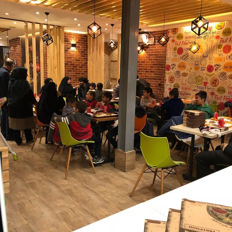 محیط گرم و دلنشین رستوران پیتزا تنوری پاروت. خانواده‌ها و کودکان از فضای داخلی شلوغ و غذای فست فود لذت می‌برند.