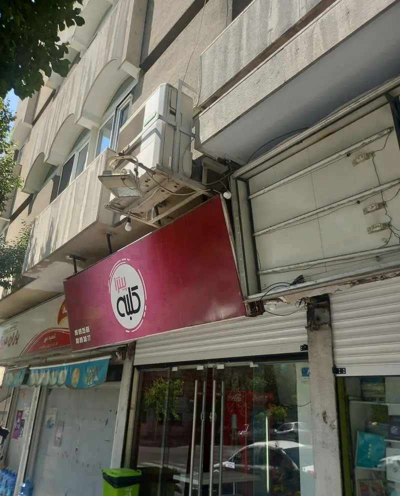 نمای بیرونی کسب و کار پیتزا کلبه با تابلوی قرمز رنگ. شماره‌های تماس 88892565 و 88893077 برای سفارش انواع پیتزا و فست فود.