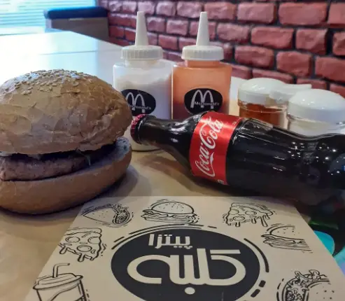 سفارش برگر و نوشیدنی کوکاکولا در فست فود پیتزا کلبه، به همراه سس‌های مخصوص و منوی جذاب برای تجربه یک غذای لذیذ.