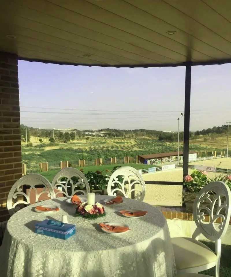 فضای باز و دنج رستوران ایرانی باراد با میز چیدمان شده، منظره پیست اسب‌سواری و طبیعت سبز، برای تجربه‌ای خاص.