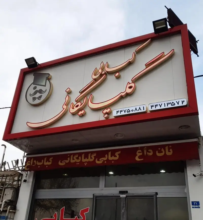 کبابی گلپایگانی، تابلوی اصلی فروشگاه با نام و آدرس، همراه با لوگوی سرآشپز و شماره تلفن‌ها. ارائه کباب داغ و نان تازه.