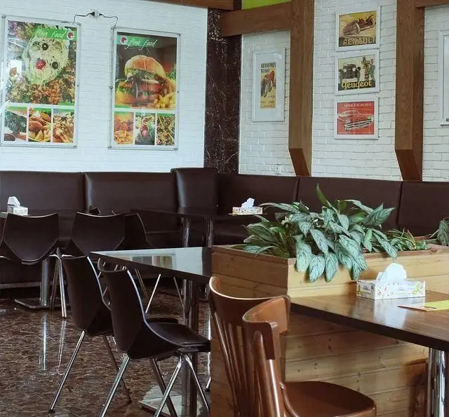 فضای داخلی شیک فست فود فینا فود با نیمکت‌های چرم قهوه‌ای، میزهای مدرن، دیوار آجری سفید، پوسترهای غذا و گیاهان آپارتمانی.