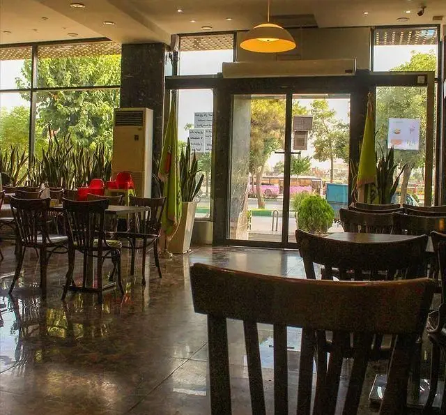 نمای داخلی کافه فینا فود، محیطی روشن با میزهای چوبی، گلدان‌های سانسوریا و پنجره‌های بزرگ رو به فضای سبز و خیابان. تجربه‌ای دلنشین.