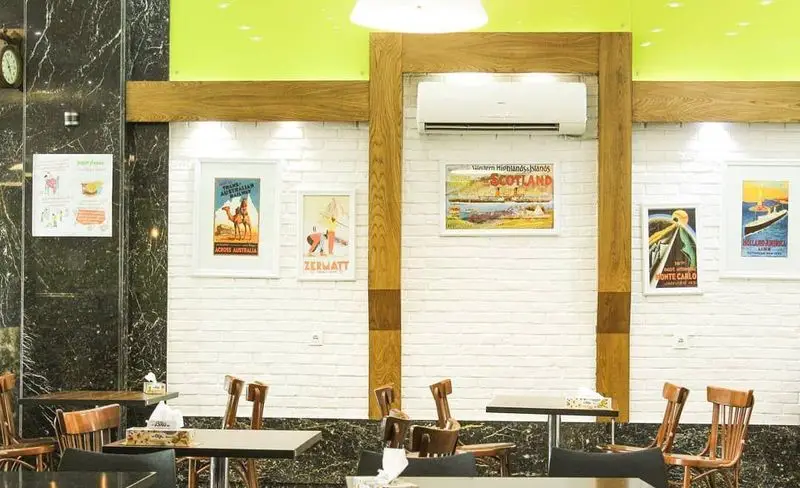 دکوراسیون داخلی مدرن و دلپذیر رستوران فینا فود با میزهای چوبی، صندلی‌های شیک و دیوارهای آجری سفید تزئین شده با تابلوهای سفر.