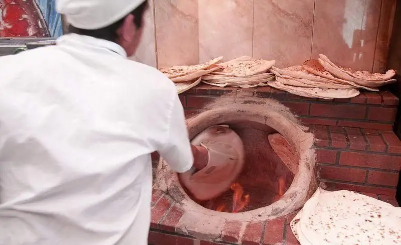 شاطر رستوران توچال کباب در حال تهیه نان داغ و سنتی در تنور. لذت کباب تازه با نان تنوری، تجربه‌ای اصیل و به یادماندنی.