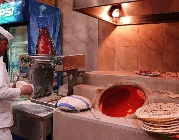 آشپز رستوران توچال کباب در حال پخت نان داغ سنتی در تنور، صحنه‌ای دلنشین از نانوایی و آماده‌سازی نان تازه برای کباب.