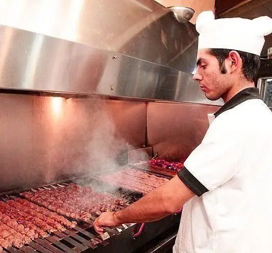 سرآشپز رستوران توچال کباب با کلاه سفید، در حال گریل کردن کباب کوبیده‌های تازه و لذیذ بر روی منقل حرفه‌ای و دودزا.