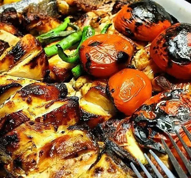 نمای نزدیک از غذای خوشمزه رستوران توچال کباب شامل ماهی کبابی، گوجه کبابی، فلفل سبز و انواع کباب‌های لذیذ دیگر. تجربه‌ای دلپذیر از غذای ایرانی.