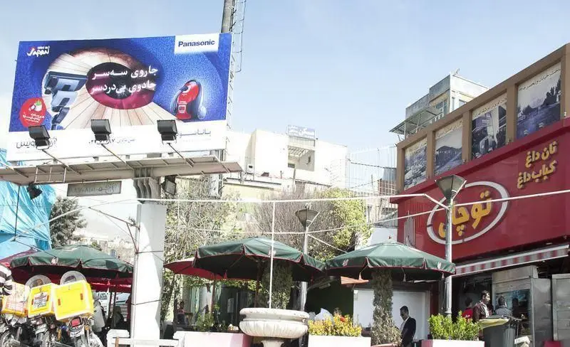 رستوران توچال کباب با تابلو "نان داغ کباب داغ"، فضای باز دلنشین برای مشتریان و موتورسیکلت‌های آماده تحویل سفارش در تهران.