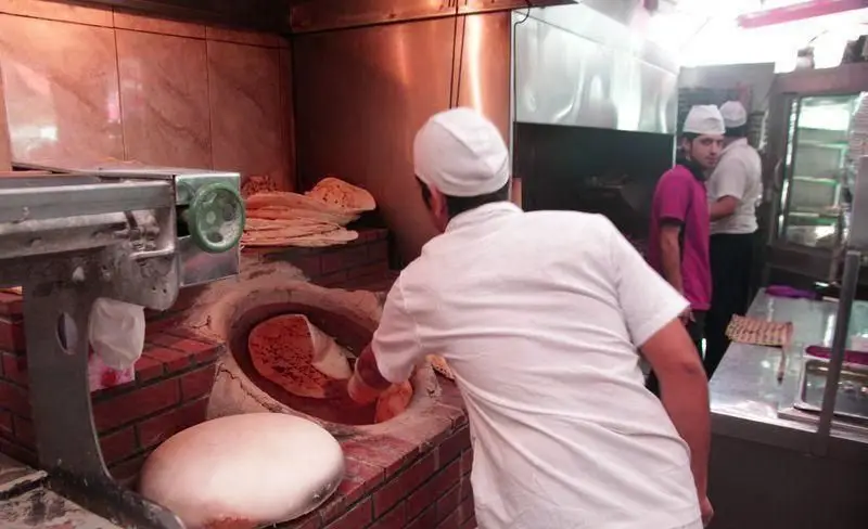 نانوایی رستوران توچال کباب: نانوای مشغول پخت نان داغ در تنور سنتی، همراه با خمیر آماده و پشته نان‌های تازه پخته شده.