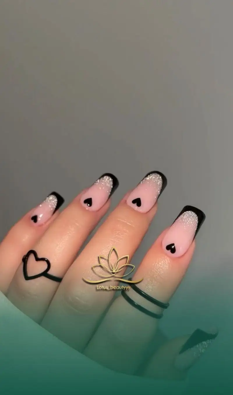 طراحی ناخن شیک و دخترانه با لاک صورتی ملایم، فرنچ مشکی اکلیلی و طرح قلب‌های کوچک مشکی در سالن زیبایی لوتوس بیوتی