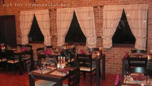 فضای داخلی گرم و دلنشین رستوران ایتالیایی بیسترو با دیوارهای آجری، میز و صندلی‌های غذاخوری چوبی چیدمان شده و پنجره‌های پرده‌دار.