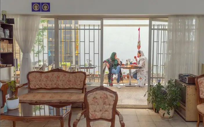 فضای داخلی کافه بالا در تهران، شامل مبلمان کلاسیک و دنج، مشرف به پاتیو با حضور دو زن در حال نوشیدن و گفتگو.