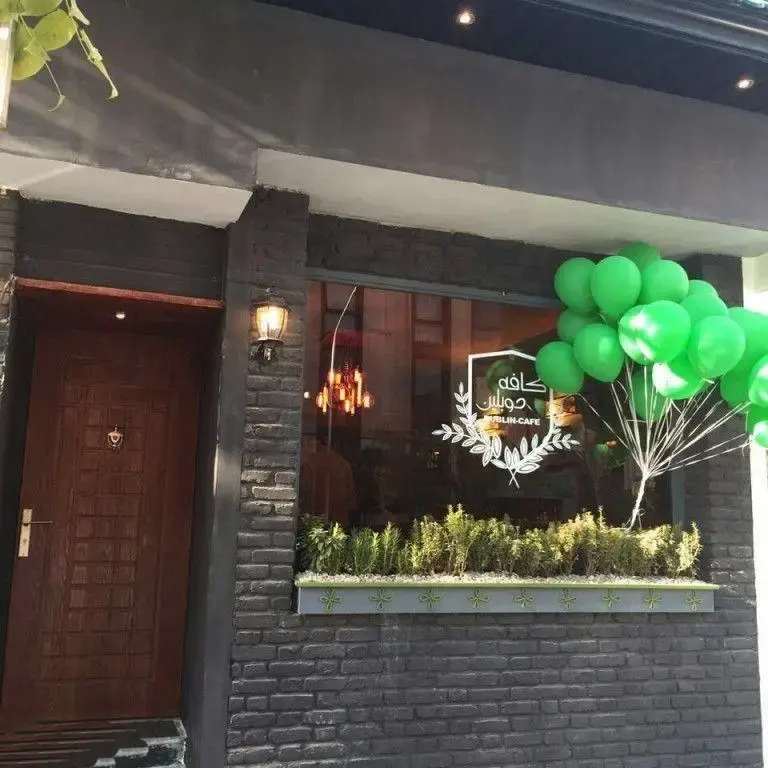 نمای جذاب و مدرن بیرونی کافه دوبلین با دیوار آجری تیره، در چوبی شیک، پنجره با گلدان گیاه و بالون‌های سبز افتتاحیه.