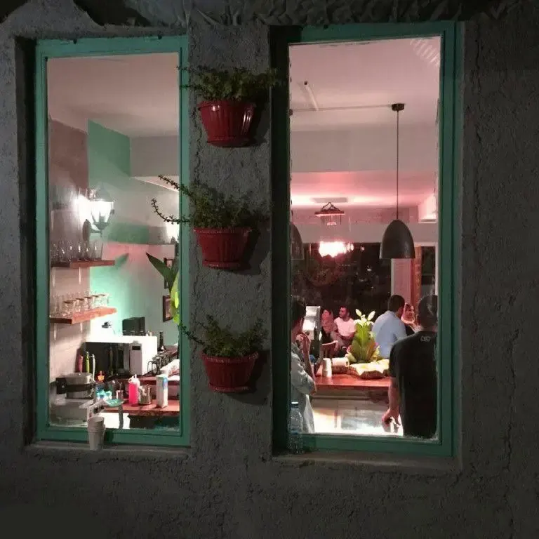 نمای بیرونی کافه دوبلین در شب، پنجره‌های روشن نشان‌دهنده مشتریان و فضای داخلی دنج، همراه با گلدان‌های تزئینی زیبا.